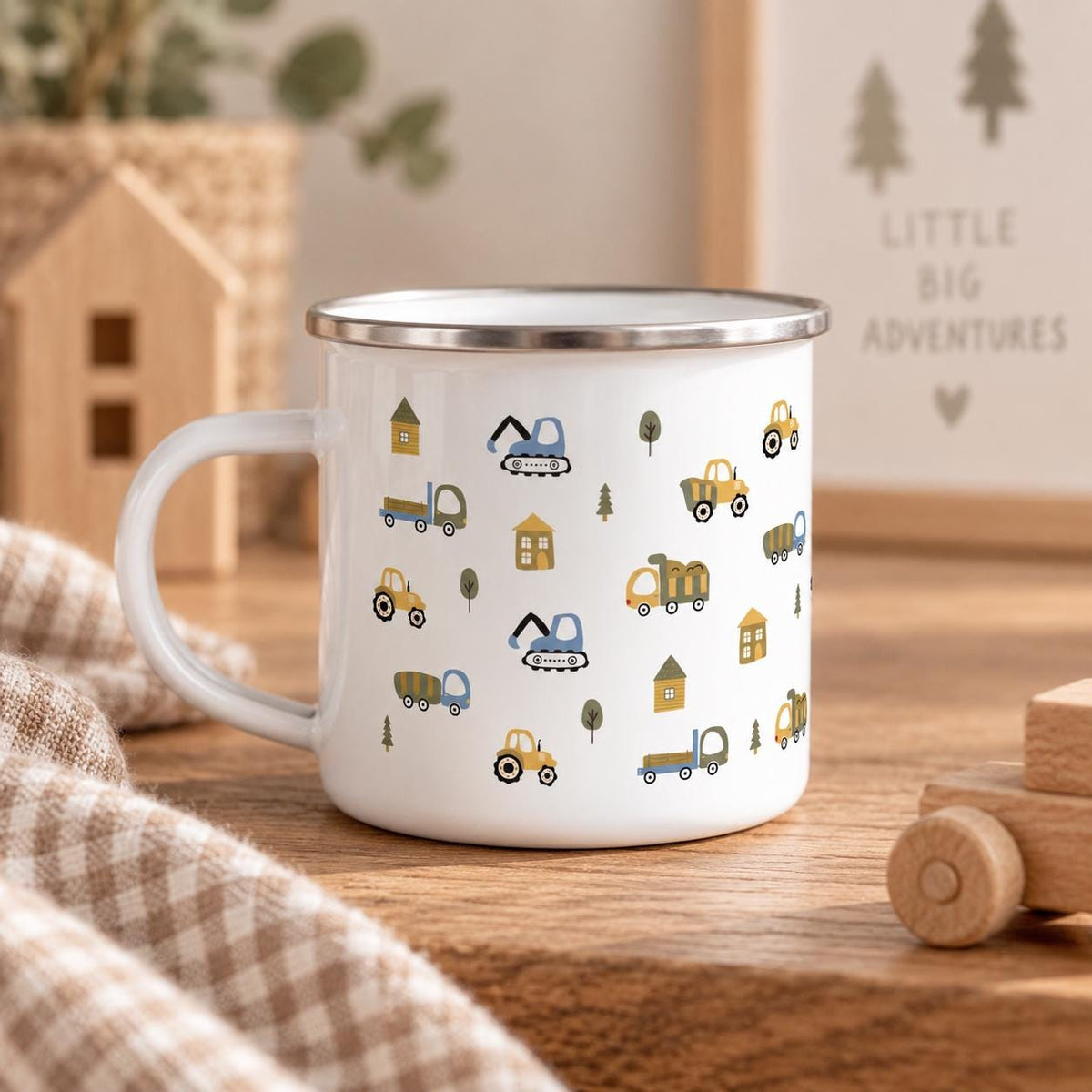A white enamel mug with a silver-toned rim and a handle, featuring a repeating pattern of small construction vehicles, including excavators, dump trucks, and tractors, interspersed with simple house and tree icons in muted colours.