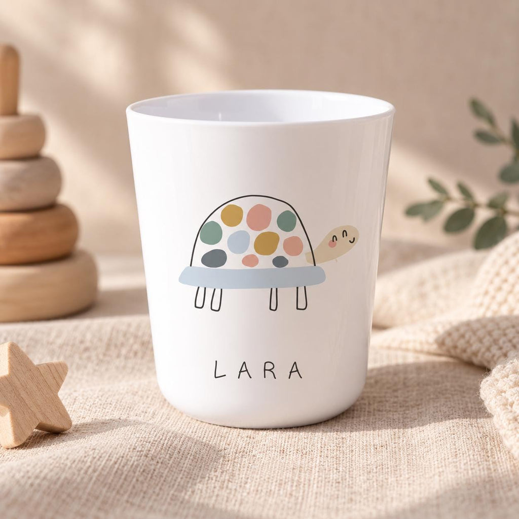 A white cup featuring a graphic illustration of a turtle with a multi-coloured spotted shell in shades of yellow, pink, blue, and grey. The name LARA is printed in black capital letters below the turtle illustration on the cup surface.