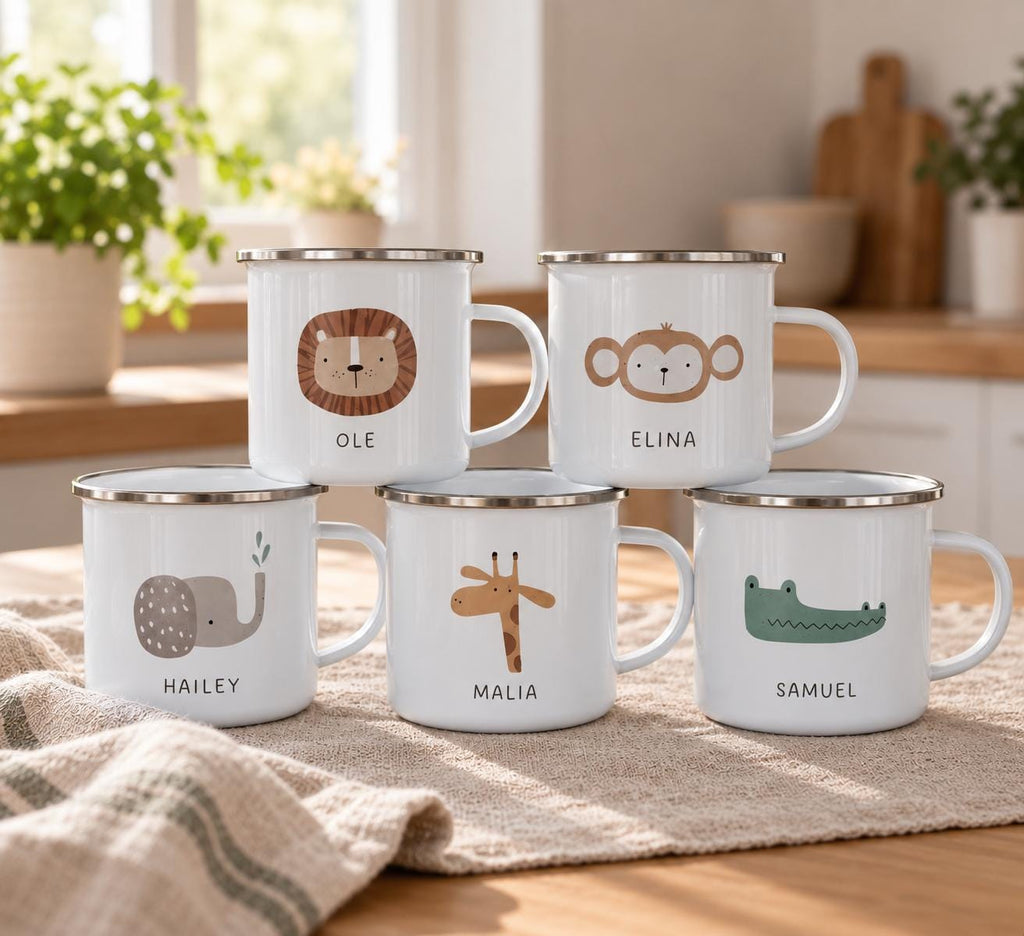 Five white metal mugs with silver rims, each featuring a unique animal illustration and a name. The mugs display a lion labelled OLE, a monkey labelled ELINA, an elephant labelled HAILEY, a giraffe labelled MALIA, and a crocodile labelled SAMUEL.