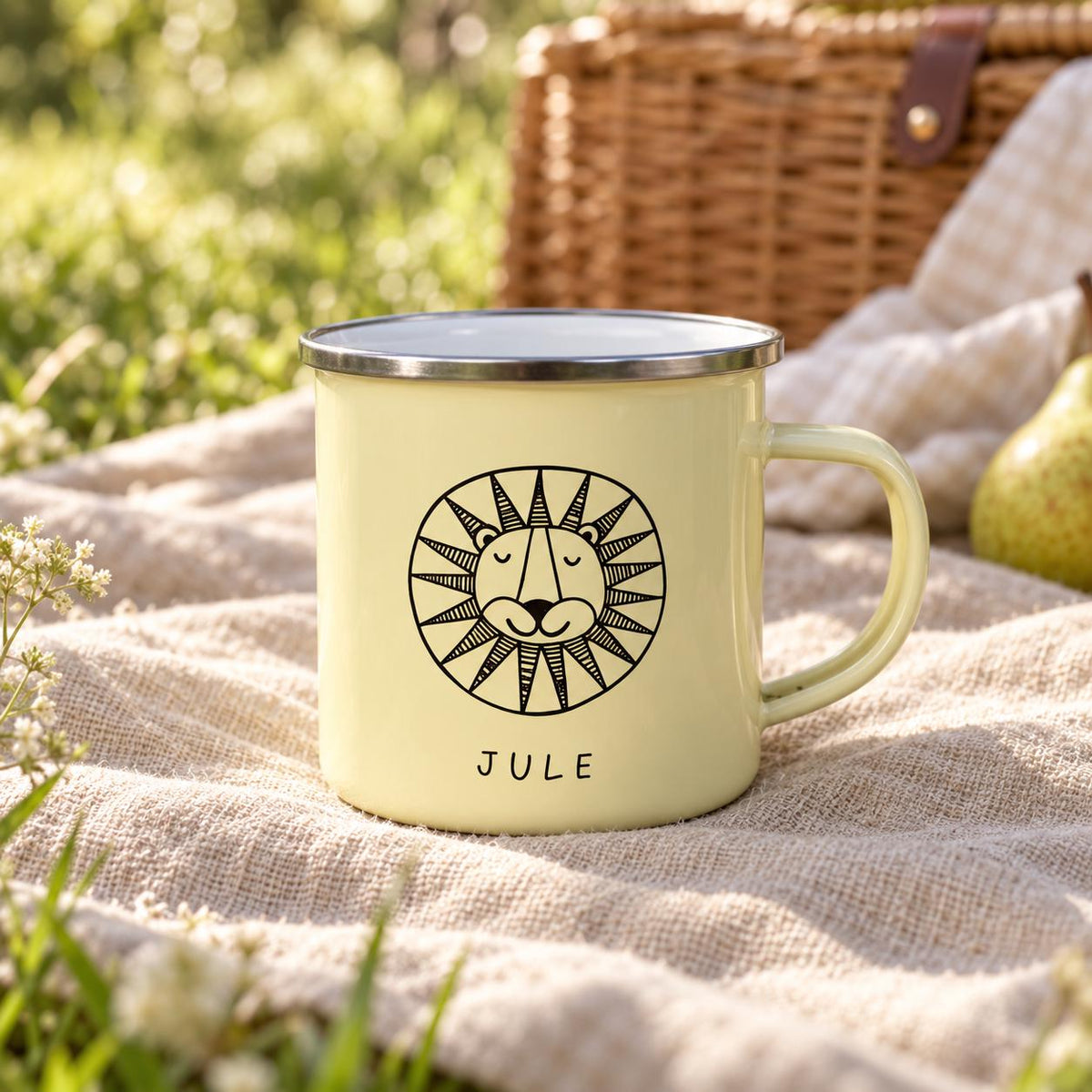 A pale yellow enamel mug with a silver rim and a handle. The front features a black line drawing of a stylised lion face with a circular mane and the name JULE printed in simple black capital letters underneath the graphic design.