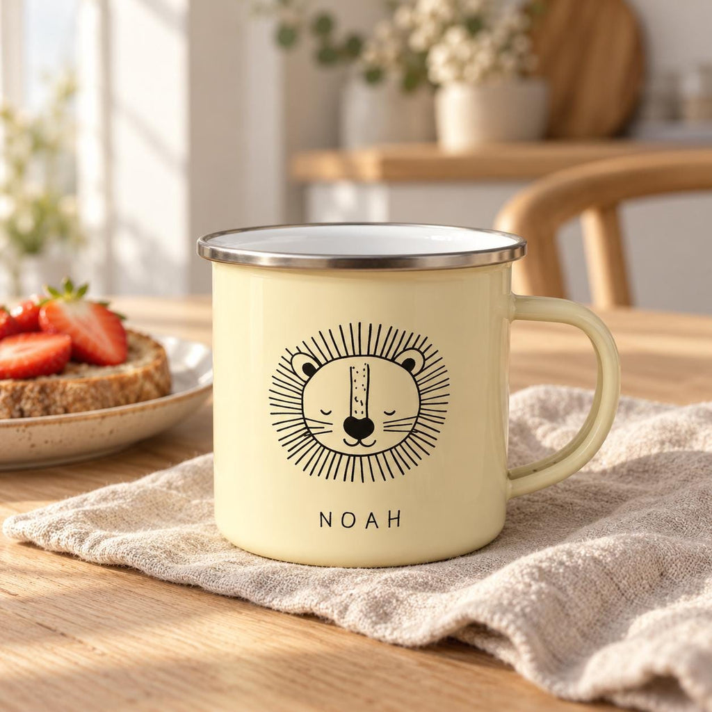 A pale yellow enamel mug with a silver rim and a handle. The front features a black line drawing of a lion's face with closed eyes and a mane, positioned above the name NOAH printed in simple black capital letters.