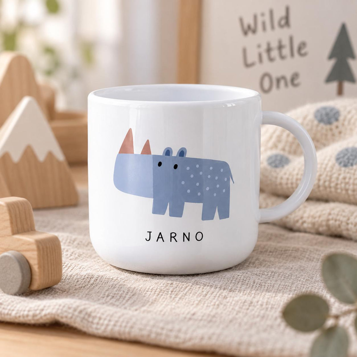 A white kids cup featuring a blue rhinoceros illustration with a dotted pattern and two small horns. The name JARNO is printed in black capital letters below the rhinoceros. The cup has a smooth finish and a curved handle.