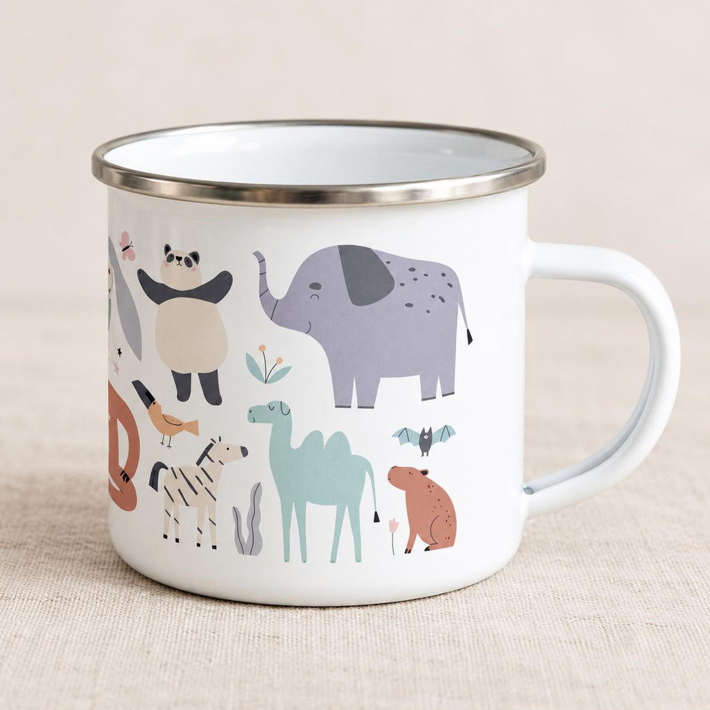 White enamel children’s mug with a silver rim and right-side handle on pale linen. The wraparound animal print shows a lavender elephant, panda, sage camel, zebra and small colourful creatures.