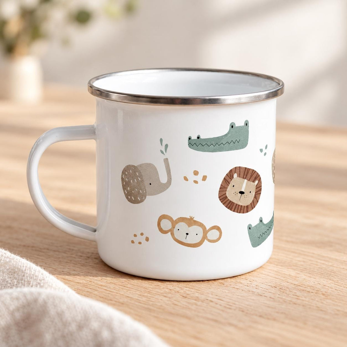 Opposite side of the white safari enamel mug, with its handle on the left and silver rim. The print shows an elephant, crocodiles, lion and monkey, photographed on pale wood beside neutral linen.