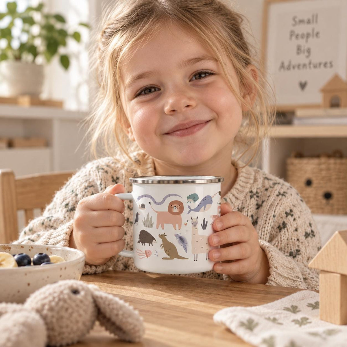 A white enamel mug featuring a colourful pattern of various animals including a lion, a kangaroo, a llama, and a whale, finished with a silver-toned metal rim and a sturdy handle, designed for holding beverages in a simple, functional style.