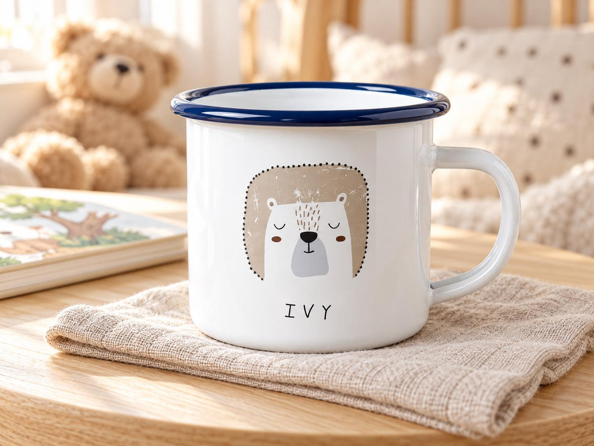 Personalised bear kids mug with a navy rim and the name IVY, on a muslin cloth beside a teddy bear and a picture book.