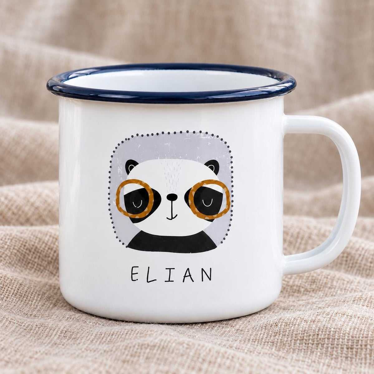 Personalised panda kids mug: white enamel mug with a navy rim, showing a panda wearing round glasses and the name ELIAN, on a soft beige blanket.