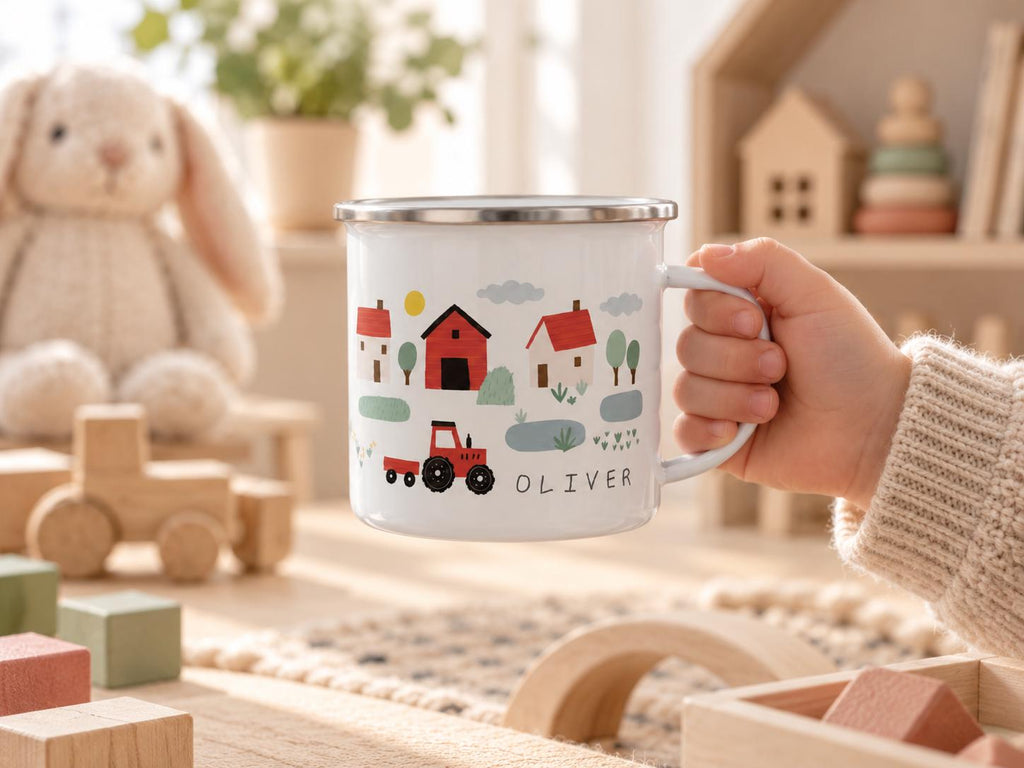 A white enamel mug with a silver rim featuring a colourful farm scene illustration including a red barn, houses, trees, and a red tractor. The name OLIVER is printed in black capital letters on the side of the mug near the handle.