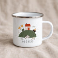 A white enamel mug with a silver rim and a handle, featuring a printed farm scene with a house, a cow, a tractor, and haystacks. The name OLIVER is printed in black capital letters below the green hill illustration on the mug.