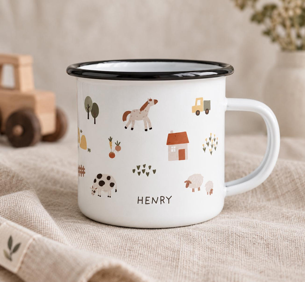 A white enamel mug with a black rim and handle, featuring a repeating pattern of farm animals, trees, a house, and a truck. The name HENRY is printed in black capital letters on the front of the mug below the cow illustration.