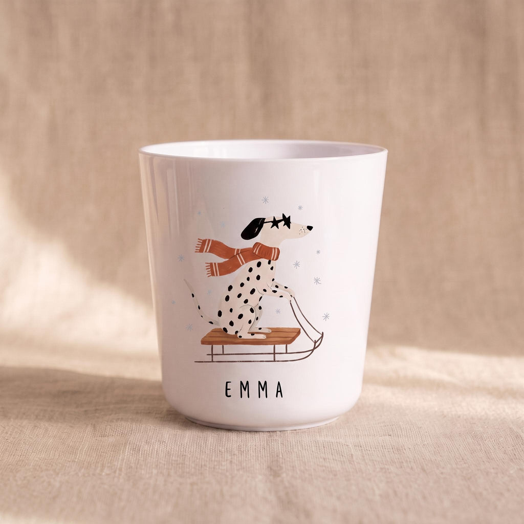 A single white child's cup featuring an illustration of a dalmatian wearing a scarf and riding a sled, with the name Emma printed below.