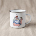 A white enamel camping mug featuring an illustration of a bearded man in a striped shirt holding a cup and a pastry, with the text Fika above him.