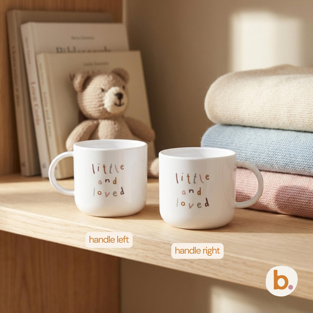 Two white mugs printed with little and loved on a wooden shelf next to stacked knit blankets and a toy bear.