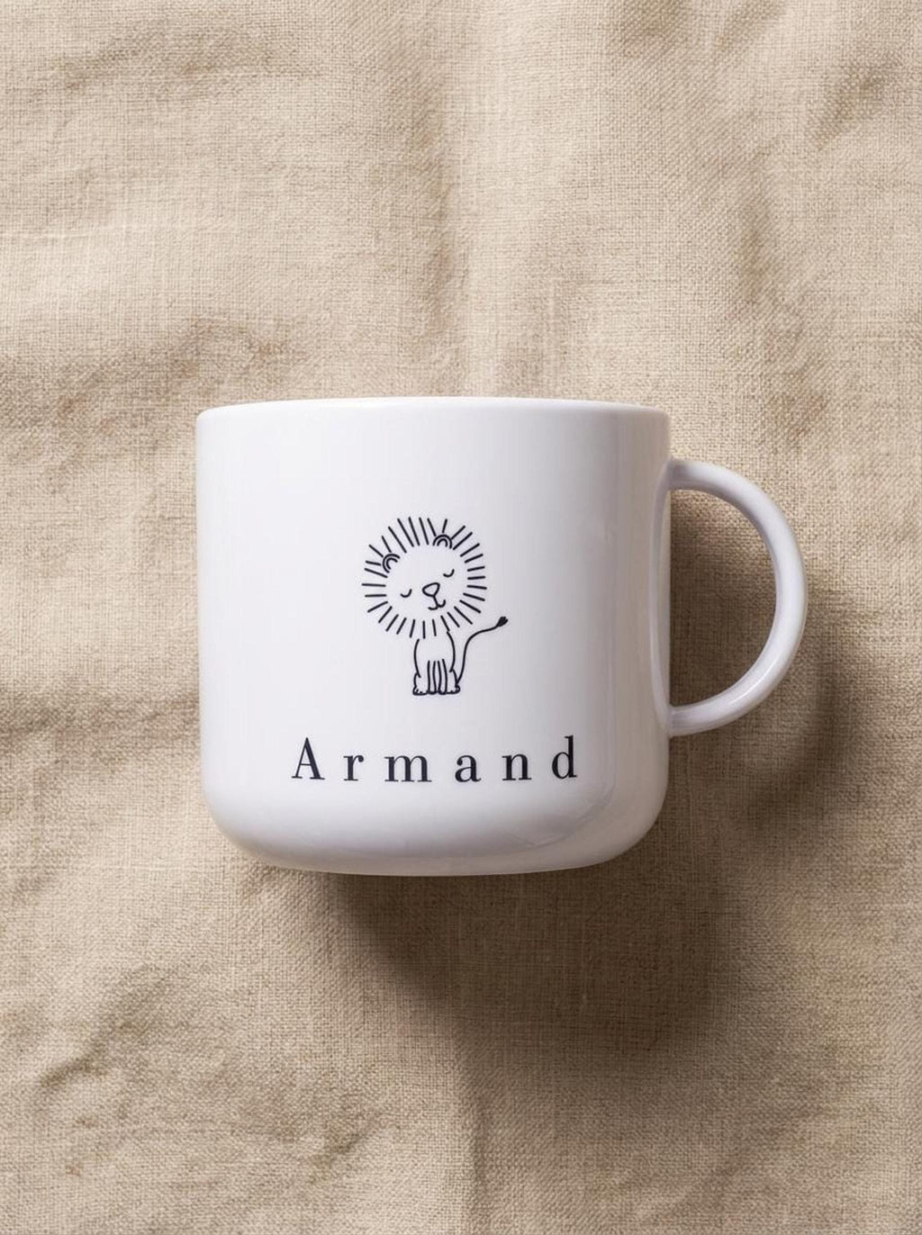 A white polymer cup featuring a line-art lion and the name Armand rests on a neutral-toned linen cloth.