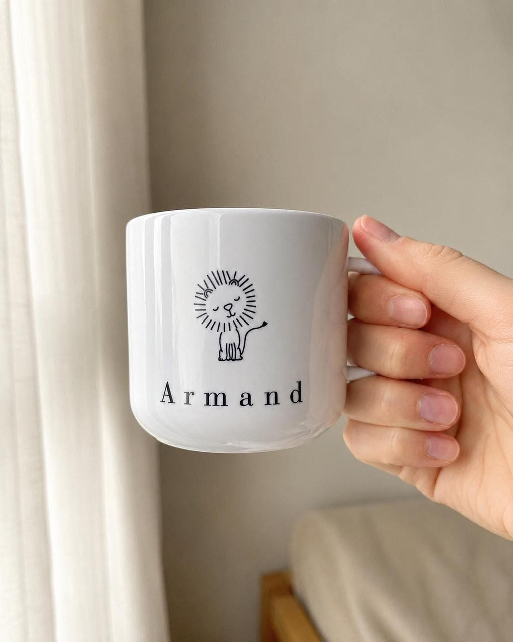 A person's hand holds the white polymer mug, displaying the black line illustration of a lion and the text Armand.