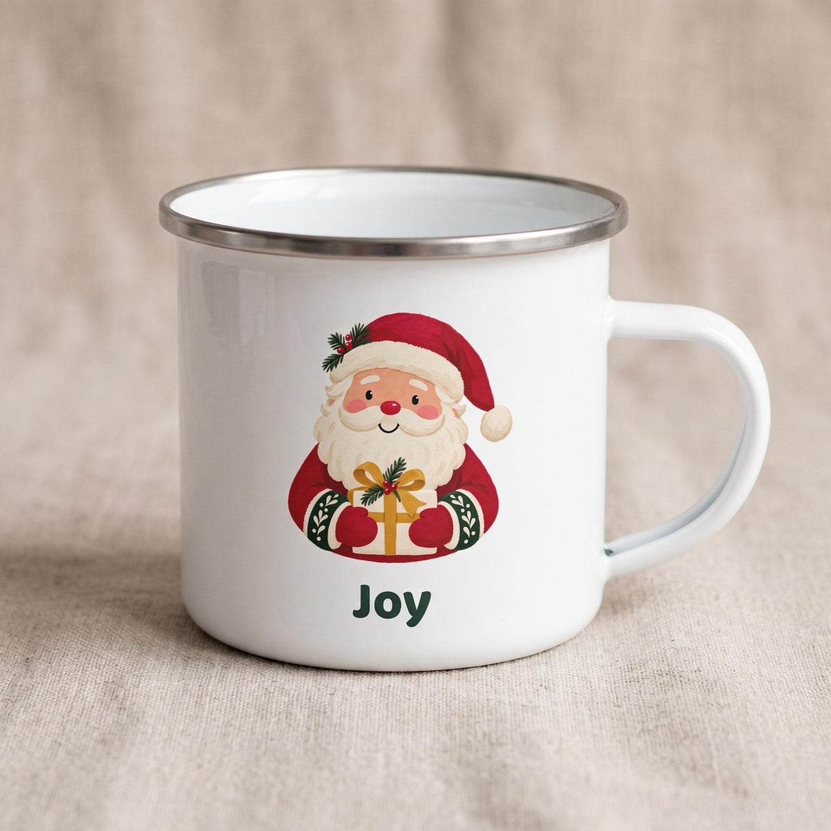 A white enamel mug with a silver metal rim shows a Santa Claus graphic holding a gift, with the name Joy printed below.
