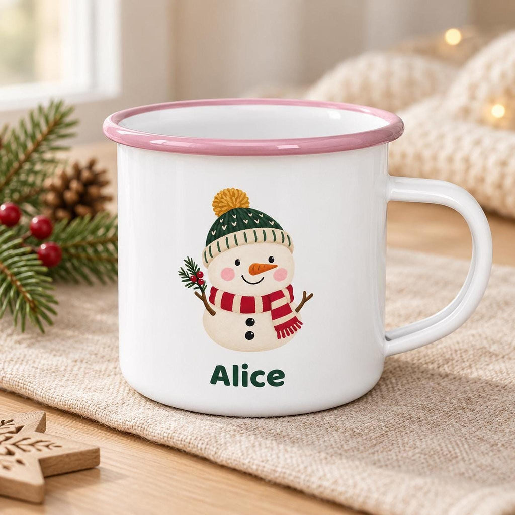 A white enamel mug with a pink rim features a snowman illustration wearing a green hat and red scarf, with the name Alice printed below.