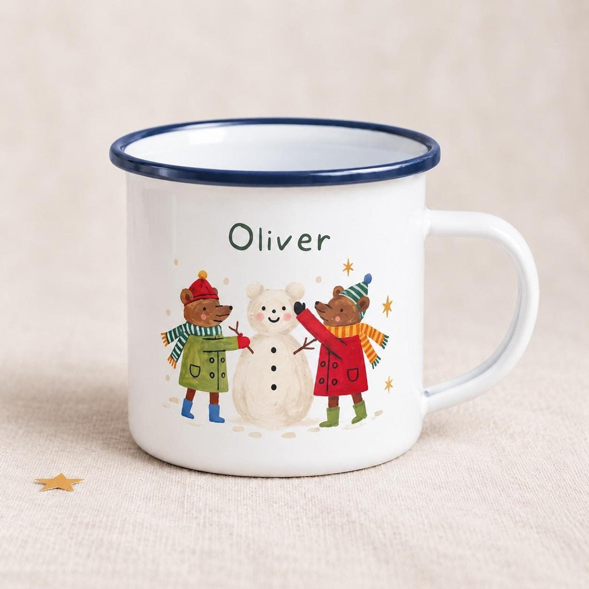 A white enamel mug with a dark blue rim featuring the name Oliver above an illustration of two bears making a snowman.