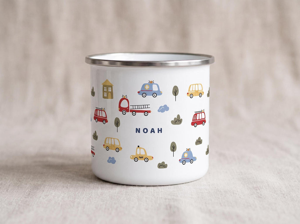 A white enamel mug featuring a pattern of colorful emergency vehicles and trees, with the name Noah printed in blue.