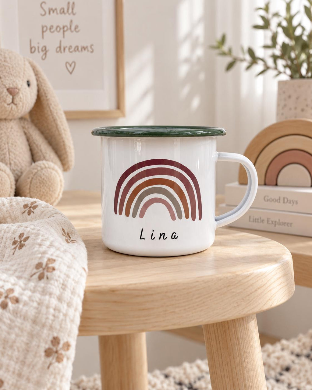 A white enamel mug with a dark green rim, featuring a printed graphic of a multi-coloured rainbow in shades of maroon, terracotta, and sage green. The name Lina is printed in black, lowercase, sans-serif lettering below the rainbow.