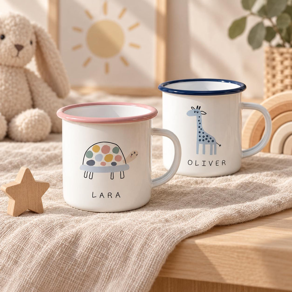Two white enamel mugs with handles. One mug features a colourful turtle illustration and the name LARA in black text with a pink rim. The second mug features a blue giraffe illustration and the name OLIVER in black text with a blue rim.