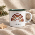 A white enamel mug with a dark green rim and a handle. The front features a graphic of a multi-coloured rainbow in shades of brown, rust, and pink. Below the rainbow, the name Lina is printed in a simple, black, sans-serif font.