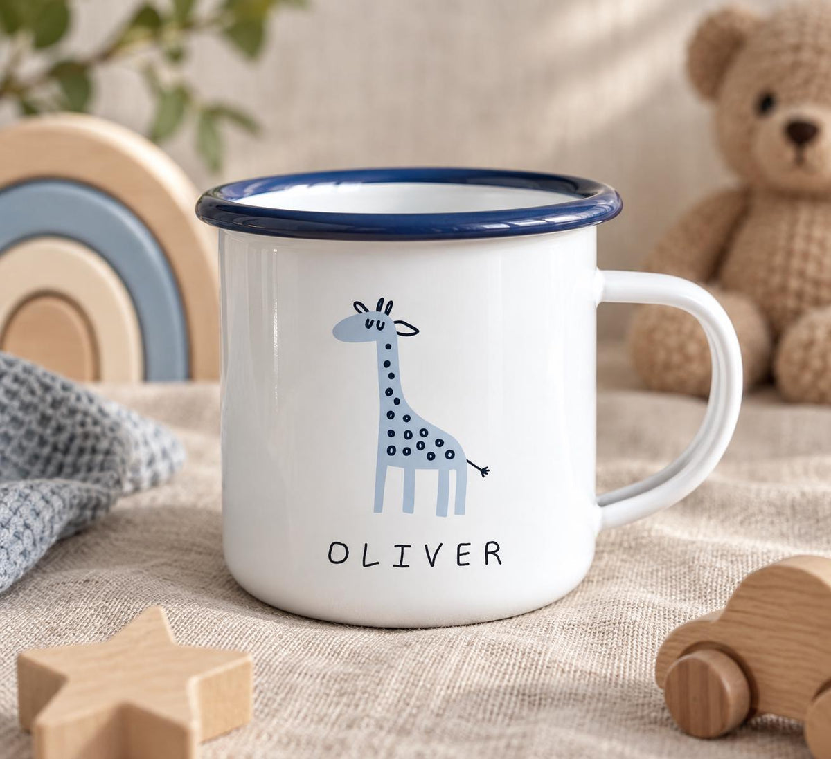 A white enamel mug with a dark blue rim and handle, featuring a light blue giraffe illustration and the name OLIVER printed in black text on the front. The mug has a smooth, glossy finish and a simple cylindrical shape.