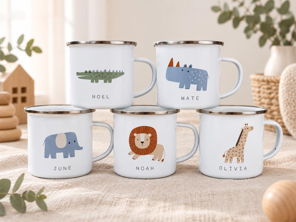 Five white enamel mugs with silver rims, each featuring a unique animal illustration and a name printed below. The animals include a green crocodile labelled NOEL, a blue rhino labelled MATE, a blue elephant labelled JUNE, a lion labelled NOAH, and a giraffe labelled OLIVIA.