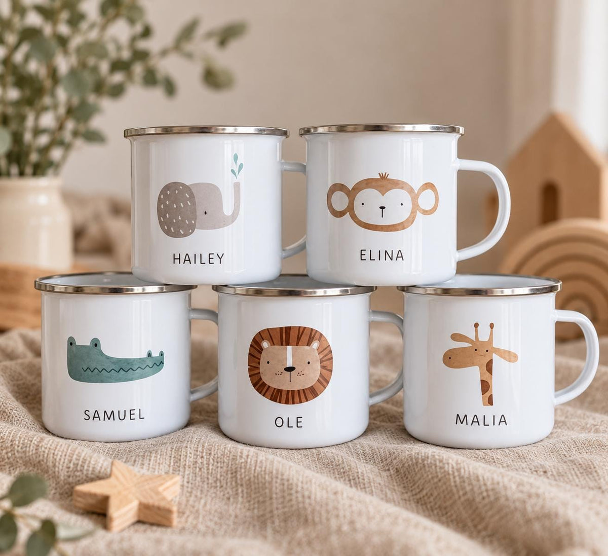Five white metal mugs with silver rims, each featuring a unique animal illustration and a name printed below. The animals include an elephant labelled HAILEY, a monkey labelled ELINA, a crocodile labelled SAMUEL, a lion labelled OLE, and a giraffe labelled MALIA.