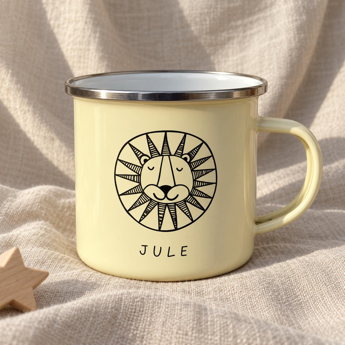 A pale yellow enamel mug with a silver-toned rim and a handle. The front features a black line drawing of a lion's face inside a circular sun-like mane. Below the lion illustration, the name JULE is printed in black capital letters.