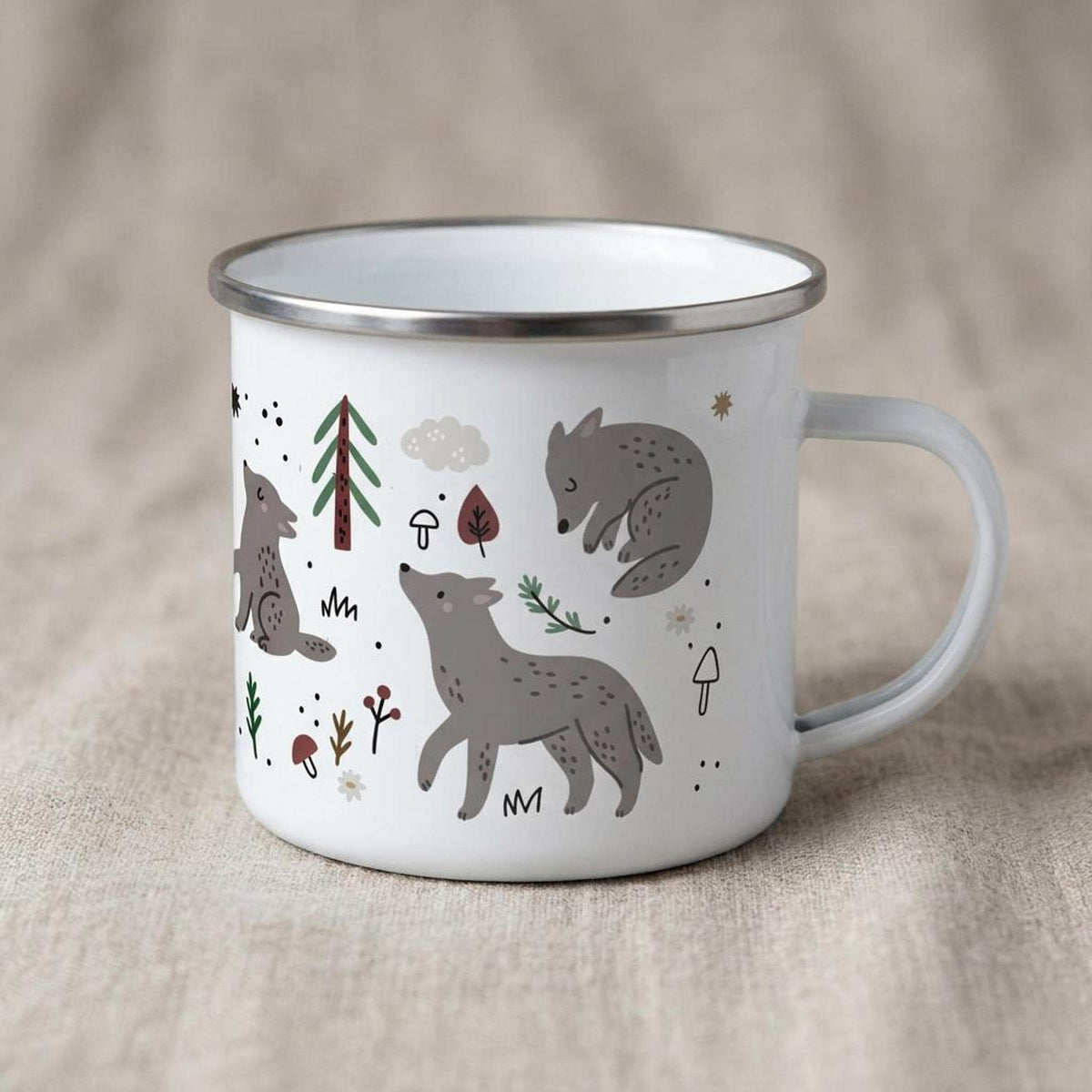 A white camp mug with woodland wolf illustrations rests on a neutral textile surface.