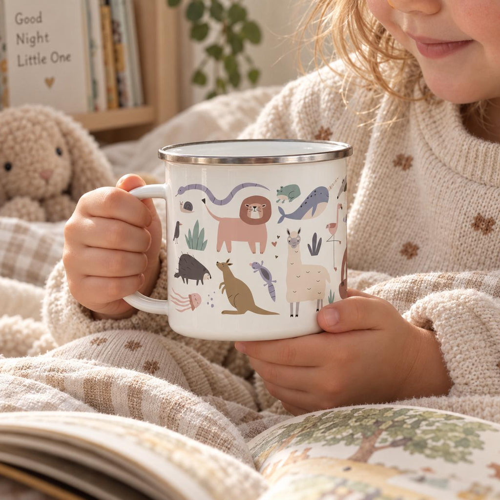 A white enamel mug with a silver rim featuring a colourful pattern of various animals including a lion, kangaroo, llama, whale, and snake. The mug has a side handle and is held by two hands, showcasing a detailed illustration of wildlife.