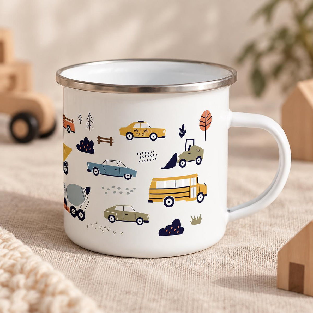 A white enamel mug with a silver rim and a handle, featuring a colourful pattern of various vehicles including a yellow taxi with the word TAXI printed on it, a yellow school bus, a blue car, a green construction vehicle, and trees.