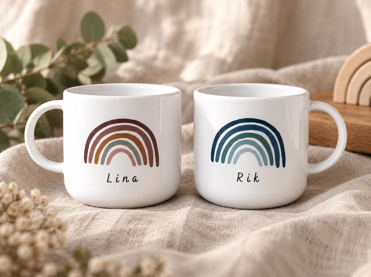 Two white kids cups with handles. The left cup features a terracotta and pink rainbow graphic with the name Lina printed below. The right cup features a navy and light blue rainbow graphic with the name Rik printed below.