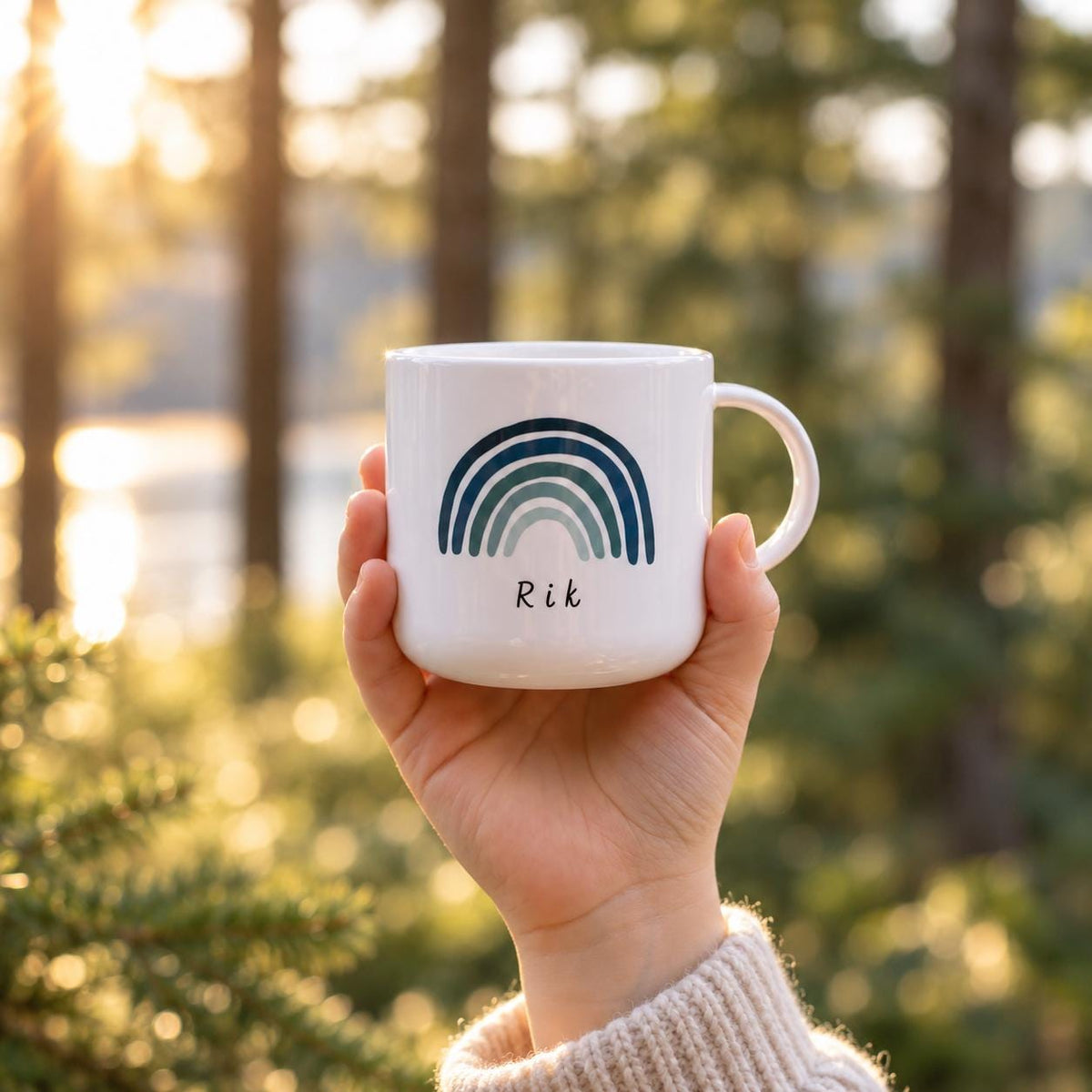 A white kids cup featuring a graphic of a multi-toned blue rainbow with the name Rik printed in black text underneath. The cup has a smooth finish, a rounded handle on the right side, and a clean, simple cylindrical shape.
