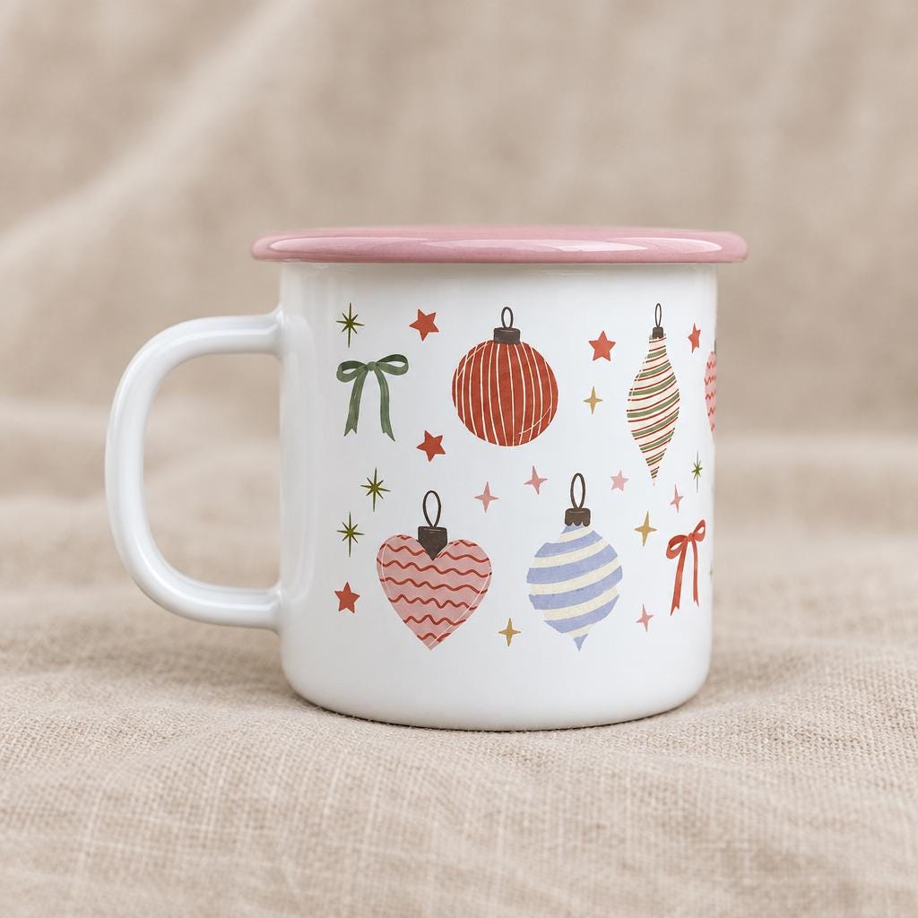 A white enamel mug with a pink rim and handle, featuring a repeating pattern of red, blue, and pink Christmas ornaments, including striped spheres, hearts, and bows, interspersed with small gold and red stars.