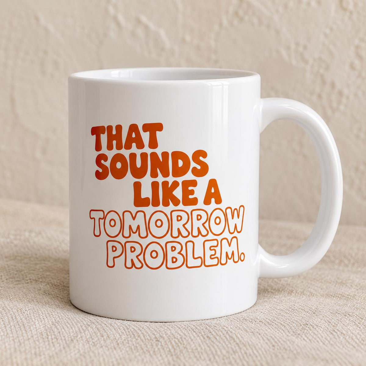 Close view of the mug printed with That Sounds Like a Tomorrow Problem in chunky burnt-orange and outlined peach letters.
