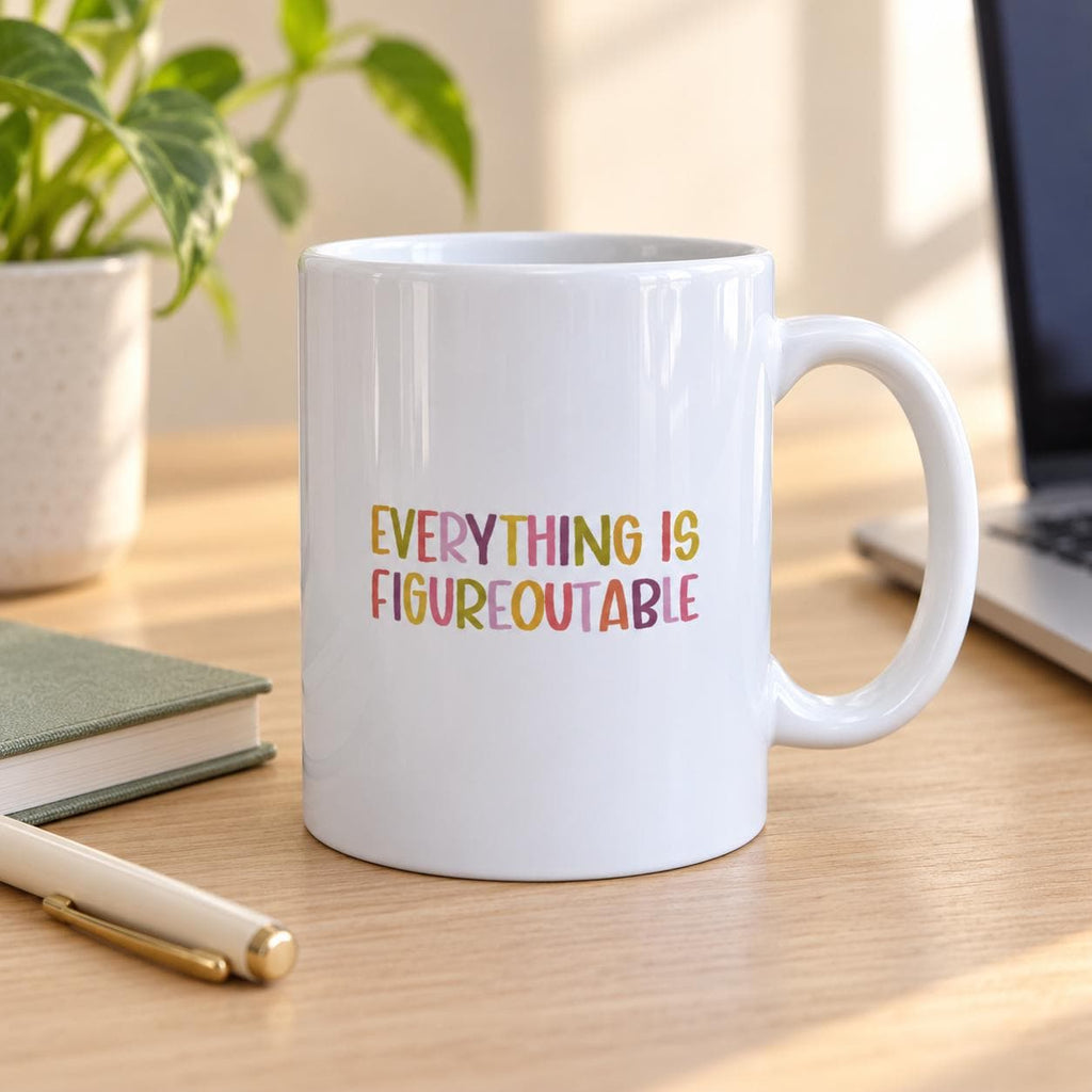 Everything Is Figureoutable mug on a wooden desk next to a laptop, notebook, pen and potted plant.